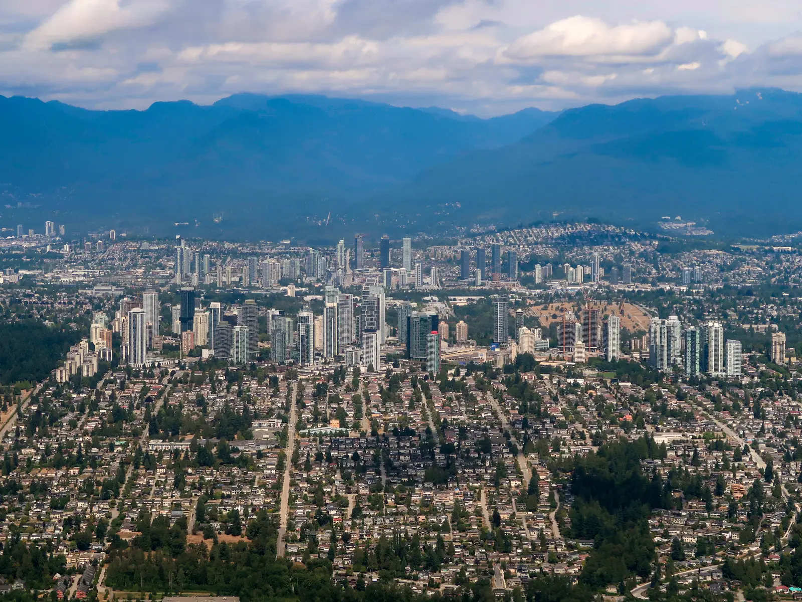 Aerial view over Burnaby residential neighbourhoods and the Metrotown skyline set against the North Shore mountains